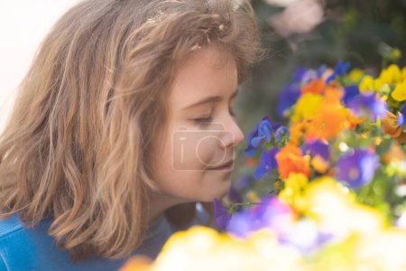 Photo for Cute blonde kid boy in spring garden. Little child under a blossom tree. Kid smelling blossom viola flowers. Kid with flower on Easter. Adorable kid in blooming cherry garden on spring day - Royalty Free Image
