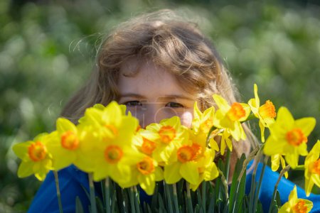 Téléchargez les photos : Petit enfant sentant le printemps narcisse fleur en plein air. Jeux d'enfants au jardin de printemps. Visage d'enfant près du cerisier en fleurs. Enfant heureux pendant la floraison printanière - en image libre de droit