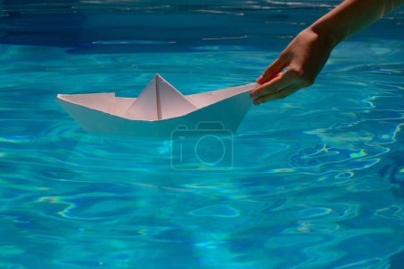 Foto de Mano femenina sosteniendo barco de papel sobre el fondo del mar. Origami barco de papel navegando en el agua causando olas y ondulaciones. Origami barco de papel - Imagen libre de derechos