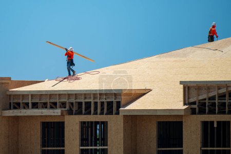 Photo for Roofing on rooftop. Builder roofer install new roof. Construction worker roofing on a large roof apartment building development. Roofer carpenter working on roof structure construction site - Royalty Free Image