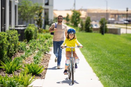 Photo for Father and son in bike helmet for learning to ride bicycle at park. Father helping son cycling. Father and son on the bicycle on summer day. Little son trying to ride bike with father. Fathers day - Royalty Free Image