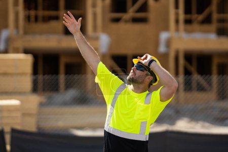Téléchargez les photos : Ouvrier sur la construction du bâtiment. Travailleur sur le chantier de construction dans le travail du casque à l'extérieur. Travailleur de chantier travaillant sur le chantier. Travailleur signalant - en image libre de droit