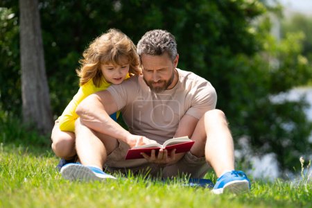 Téléchargez les photos : Père et fils lisant un livre dans le parc. Le concept d'éducation et d'amitié. Mode de vie, père a lu un livre à son mignon fils à l'extérieur, chaude journée d'été, relation familiale, enfant et parent, célibataire - en image libre de droit