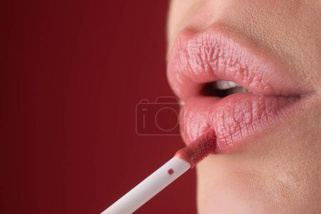 Applying lipstick. Painting lips with bright lipstick, close up. Pampering, lips correction concept. Glossy lipstick on full plump lip. Woman hand applying lipstick