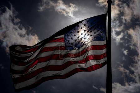 Foto de Bandera de Estados Unidos. ondeando bandera americana en el cielo oscuro y dramático. Bandera de EE.UU. ondeando cerca del sol - Imagen libre de derechos
