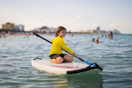 Child swimming on paddle board. Water sports, active lifestyle. Kid paddling on a paddleboard in the ocean. Child Paddle boarder. Summer Water sport, SUP surfing. Summer beach vacation