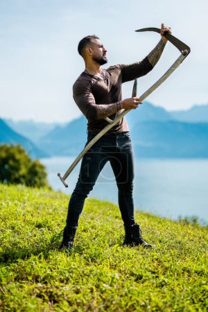 Photo for Strong farmer using scythe. Sexy Farmer with a scythe on green grass field. Muscular Farmer cut grass. Rural farmer on summer meadow mowing grass with classic traditional scythe - Royalty Free Image