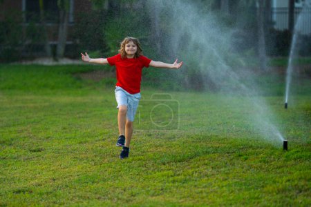 Photo for Child play near automatic sprayers in the garden. Watering in the garden. Kid freshness of nature. Automatic lawn sprinkler watering grass. Garden irrigation system watering lawn. Sprinkler system - Royalty Free Image
