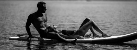 Foto de Amor de verano. Sexy pareja descansar en el tablero de paddle. Mujer sexy y el hombre descansan en el paddleboard en el agua. Estilo de vida saludable de verano. Parejas sexys. Verano caliente. Descanso. Foto en blanco y negro - Imagen libre de derechos