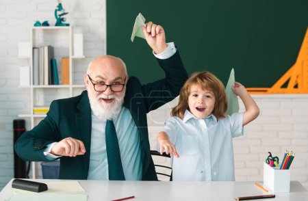 Photo for Senior teacher or grandfather and school boy pupil hold paper airplane in classroom at school. Private funny lesson - Royalty Free Image