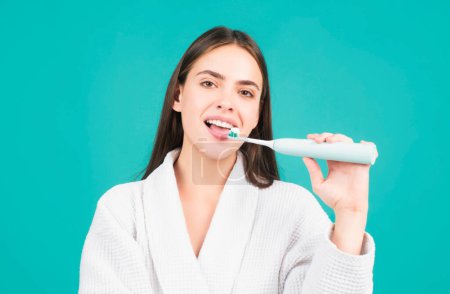 Téléchargez les photos : Jeune femme gaie brossant les dents avec une brosse à dents pendant les procédures d'hygiène matinale fond isolé, portrait du visage. Brosse à dents électrique - en image libre de droit