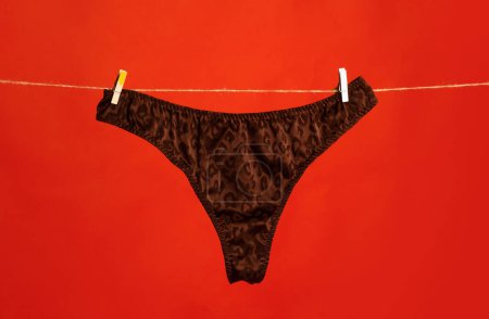 Foto de Cotton underwear. Lace underwear. Womans black erotic panties. Womens panties hanging isolated on red background - Imagen libre de derechos