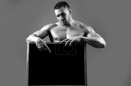 Foto de Guapo fisicoculturista con cartel publicitario. Fuerte atleta muscular sosteniendo anuncio cartel negro en blanco. Espacio de copia - Imagen libre de derechos