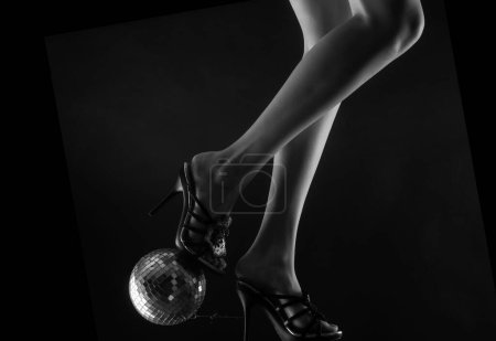 Disco and party legs. Celebrating. Disco-ball on high heels. Woman heels with gold ball. Celebrate concept