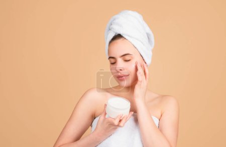 Photo for Beautiful woman with cosmetic products. Girl beauty face care. Facial treatment, cosmetology, beauty and spa. Young girl with a towel on head apply a cleansing mask cream on her face - Royalty Free Image