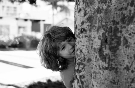 Photo for Kids active games. Playing hide and seek. Peekaboo. Little boy hiding by tree - Royalty Free Image
