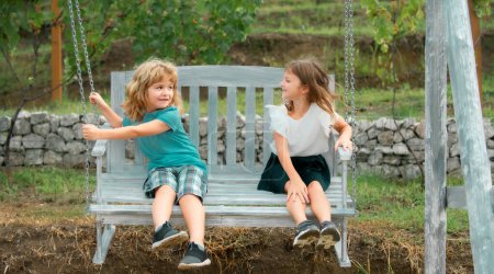 Foto de Hermano y hermana balanceándose afuera. Un niño y una niña trabajando en el jardín. Dos niños felices en el parque de verano. Concepto de vacaciones de verano para niños. Amistad de niños - Imagen libre de derechos