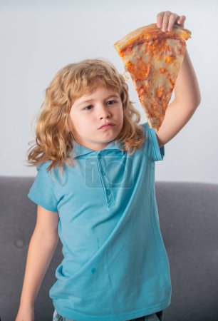 Foto de Niño comiendo pizza. Chico divertido sosteniendo rebanada de pizza cerca de la cara - Imagen libre de derechos