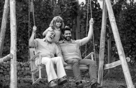 Aufgeregt spielen Vater und Sohn im Freien auf der Schaukel. Glückliche Männerfamilie. Generation der drei Männer