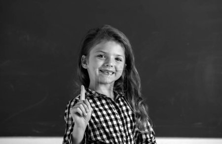 Foto de Retrato de alumna nerd escolar con expresión sorprendente apuntando con el dedo contra pizarra. De vuelta a la escuela, primer día en la escuela - Imagen libre de derechos