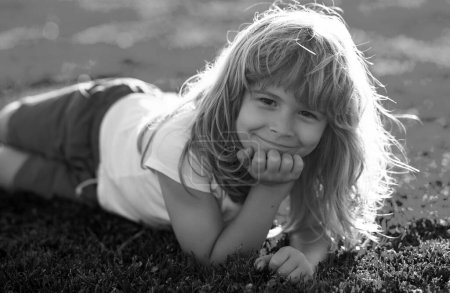 Foto de Cara de niño de verano. Niño sonriente con fondo de hierba. Feliz niño sonriente relajándose en la hierba. Niño lindo disfrutando en el campo de hierba y soñando. Lindo chico soñando despierto en un campo - Imagen libre de derechos