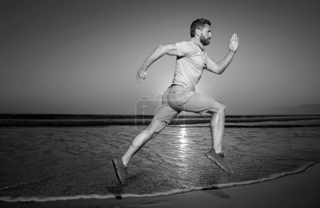 Photo for Athletic young healthy man running on sunrise seaside. Male model in sportswear exercising outdoors on sunset sea background - Royalty Free Image