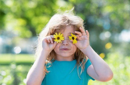Foto de Retrato de niños de primavera, cara graciosa. El niño está oliendo flores en el patio verde. Adorable niño en un prado de verano y flores que huelen - Imagen libre de derechos