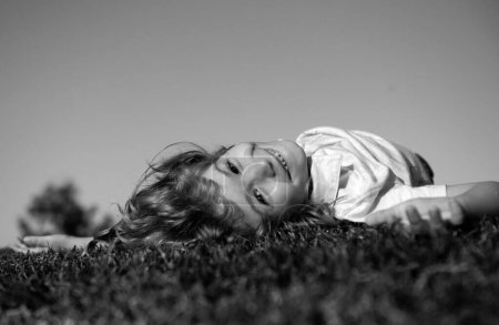 Téléchargez les photos : Garçon joyeux allongé sur l'herbe verte. Joyeux enfant jouant dans le champ de printemps vert sur fond de ciel. Concept de liberté et d'imagination - en image libre de droit
