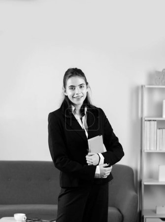 Téléchargez les photos : Jeune secrétaire attrayante femme tenant un cahier dans un lieu de travail moderne occupé dans le bureau. Jolie comptable fille dans l'intérieur du bureau - en image libre de droit