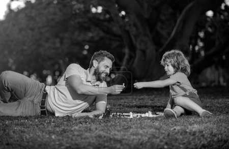 Photo for Son laying on grass and playing chess with father. Intelligent child, smart kids - Royalty Free Image