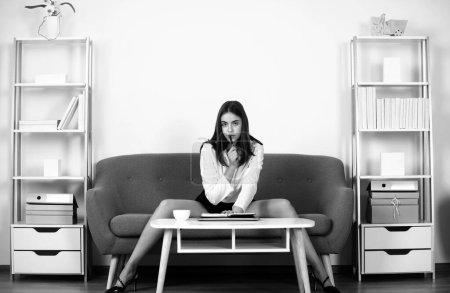 Seductive secretary with sexy legs sit on sofa in office. Sexy business woman. Sensual girl employee