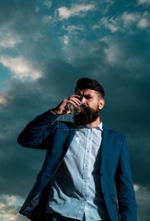 Man with beard and mustache holds alcoholic beverage on sky background. Service and alcoholism concept