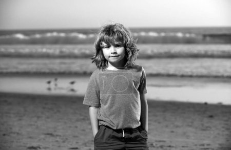 Foto de Niño en camiseta caminando en la playa de verano. Niños mano en bolsillo - Imagen libre de derechos