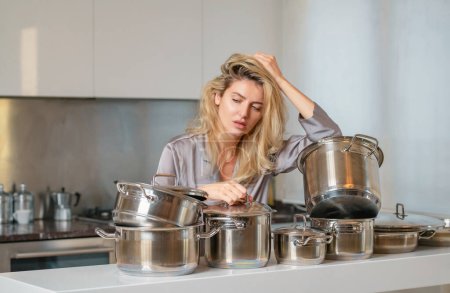 Téléchargez les photos : Femme ennuyée avec beaucoup de casseroles dans la cuisine le matin. Matin de femme femme au foyer - en image libre de droit
