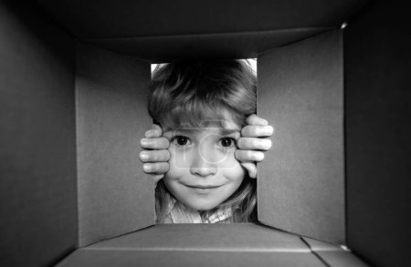 Téléchargez les photos : Child open paper cardboard box. Kid boy unpacking and opening carton box looking inside with surprise face. Parcels and delivery - en image libre de droit