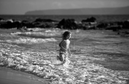 Foto de Un niño feliz corriendo en la playa tropical. Niño jugando olas de mar en el mar de vacaciones en las vacaciones de verano. Niño en la naturaleza en la orilla del mar. Niños caminando en la playa - Imagen libre de derechos