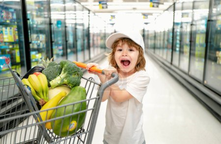 Téléchargez les photos : Petit garçon avec sac à provisions au supermarché. Shopping d'enfants dans un supermarché. Supermarché, Shopping avec enfant - en image libre de droit