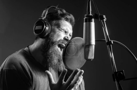 Photo for Singing man in a recording studio. Expressive bearded man with microphone. Sound producer. Karaoke signer, musical vocalist - Royalty Free Image
