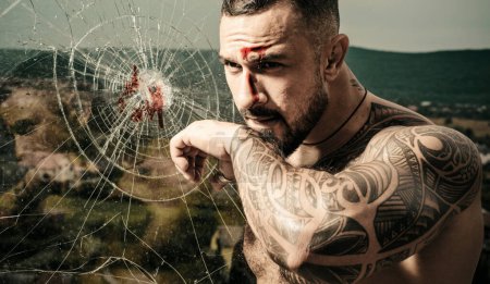 Photo for Brutal man wiping blood after hit. Strong man near the broken glass. Face with a scar - Royalty Free Image