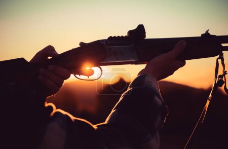 Rifle Hunter Silhouetted en Beautiful Sunset. Cazador con Fusil Poderoso con Alcance Spotting Animals. Apretó el gatillo de la escopeta. Rastrear
