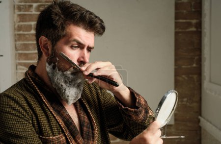 Téléchargez les photos : Concept de salon de coiffure. Coiffeur fait coiffure un homme avec une barbe. Client barbu en visite chez le coiffeur. Soin de la barbe. Homme âgé visitant coiffeur dans le salon de coiffure - en image libre de droit