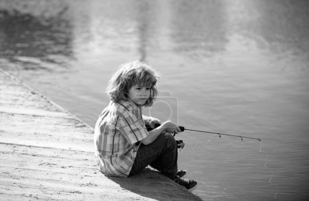 Téléchargez les photos : Un jeune pêcheur. Pêche des enfants au bord de la rivière, activités de plein air estivales. Petit garçon pêchant au bord de la rivière avec canne - en image libre de droit