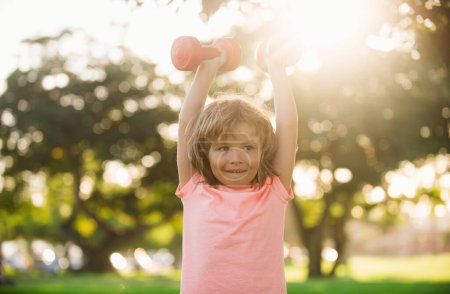Photo for Funny boy workout in park. Kids sport. Child exercising with dumbbells. Sporty and fitness child with dumbbell outdoor. Kids sport. Kids active healthy lifestyle - Royalty Free Image