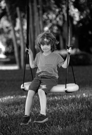 Foto de Niño jugando al aire libre. Los niños se balancean en el patio. Feliz lindo niño balanceo y divertirse saludable actividad de vacaciones de verano - Imagen libre de derechos
