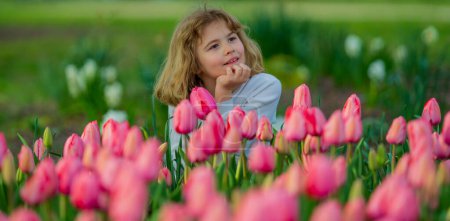 Téléchargez les photos : Gros plan portrait extérieur d'un enfant dans un parc de tulipes. Vacances de printemps. Des tulipes puantes au printemps. Mignon petit garçon tenir des tulipes fleurs nature. Portrait d'enfant au jardin de printemps avec tulipes - en image libre de droit