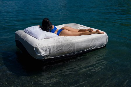 Photo for Sexy woman sleeping or resting on a mattress in the water. Water mattress concept. Sweet dreams. Summer rest. Fit model in sexy bodysuit or swimsuit floating in the lake water. Sexy Female Body - Royalty Free Image