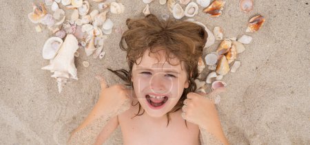 Photo for Happy Summer. Cute blonde child relax on sand. Child play with Sea shells and fine beach sand. Kid laying on sandy beach with Shells. Summer kids face - Royalty Free Image