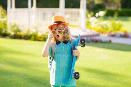 Téléchargez les photos : Enfance et mode. Enfant mignon avec skateboard sur fond de parc d'été. Enfant drôle garçon, patineur élégant tenant skateboard en plein air - en image libre de droit