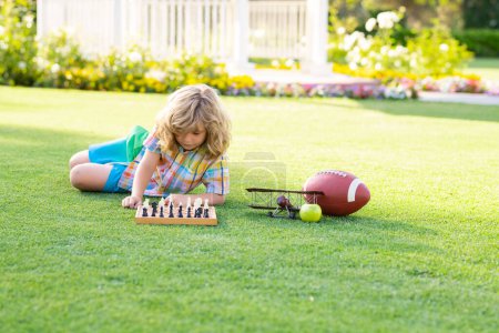 Foto de Niño jugando ajedrez y divertirse al aire libre en el patio trasero o parque de verano. Un chico listo jugando al ajedrez. Niño inteligente pensando en el ajedrez - Imagen libre de derechos