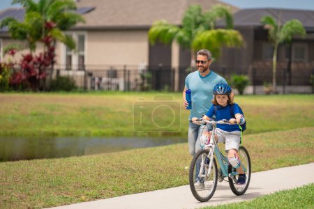 Photo for Father and son concept. Father teaching son riding bike. Father helping son to ride a bicycle in american neighborhood. Child in safety helmet learning to ride cycle with his dad. Fathers day - Royalty Free Image